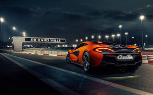 夜間在Richard Mille標誌下，橙色McLaren賽車在燈光璀璨的賽道上。