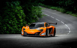 橙色McLaren賽車在彎曲的森林道路上行駛。 — 酷車 壁紙