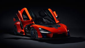 在黑暗工作室環境中，橙色McLaren Senna超級跑車打開鷗翼門。 — 麥拿侖 GIF 壁紙