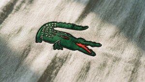 米色布料上的綠色刺繡鱷魚標誌，帶有陽光陰影。