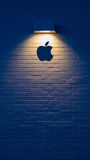 夜間，聚光燈照亮藍色磚牆上的Apple標誌輪廓。