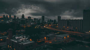 黑暗的暴風雲籠罩著城市天際線，閃爍的路燈和彎曲的高速公路在黃昏時分。 — 天際線 壁紙