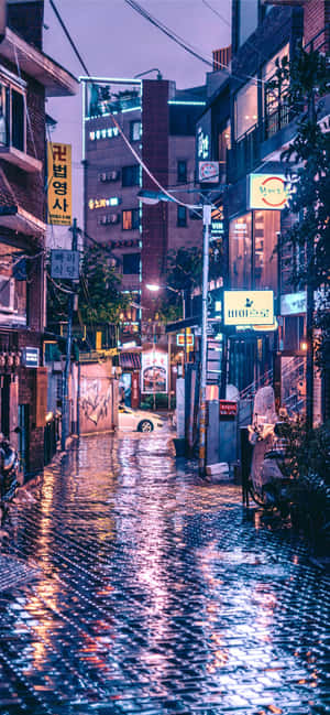 夜晚的雨中城市小巷，發光的霓虹燈招牌在濕漉漉的人行道上反射。 — OnePlus 壁紙