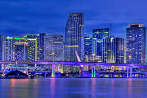 夜間城市景觀，燈火通明的摩天大樓和發光的橋樑橫跨水面。 — 邁阿密熱火 壁紙