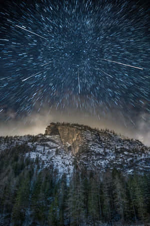 夜間積雪的山峰和森林上空的星軌