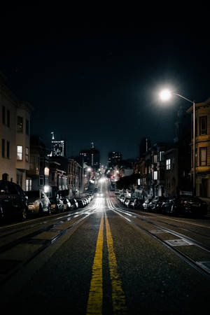 夜晚的城市街道，有停泊的汽車和發光的街燈。