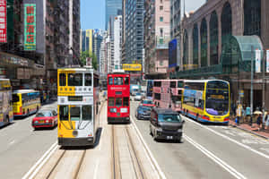 香港街道，紅色和黃色電車、巴士和汽車在高樓大廈間行駛。 — MacBook 壁紙