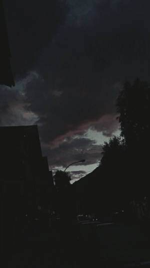 黃昏時分的黑暗城市街道，多雲的天空下建築物和樹木的剪影。 — 天空景觀 壁紙