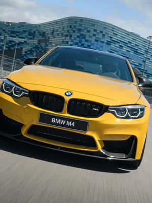 陽光明媚的日子裡，黃色BMW M4飛馳而過現代玻璃建築。