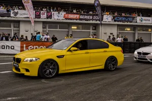 黃色BMW M5在賽車道上飄移,觀眾觀看。