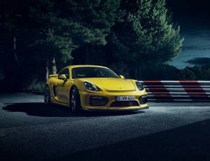 夜間賽道上的黃色保時捷 Cayman GT4，伴有樹木和護欄。