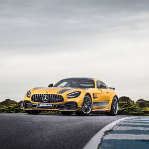 黃色 Mercedes-AMG GT R 在賽道上，配有藍色路緣石和綠色灌木叢。