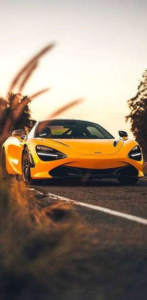 黃色McLaren跑車在日落時分的道路上疾馳，前景有模糊的草叢。