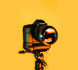 黑色Canon DSLR相機在三腳架上，黃色背景