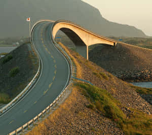 日落時分，一條彎曲的道路越過岩石地形上的橋樑，遠處山巒起伏。