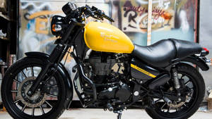 黃黑配色 Royal Enfield 電單車，在一個有塗鴉的車庫中。 — 皇室 壁紙