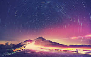 夜晚蜿蜒的山路，帶有星軌和車輛光條。