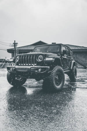 黑色Jeep Wrangler在雨中停在建築物附近的濕路面上。
