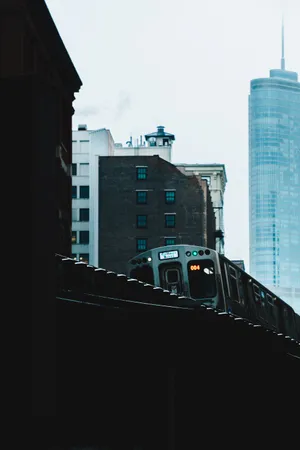 銀色地鐵列車在舊磚建築和玻璃摩天大樓之間的高架軌道上行駛。