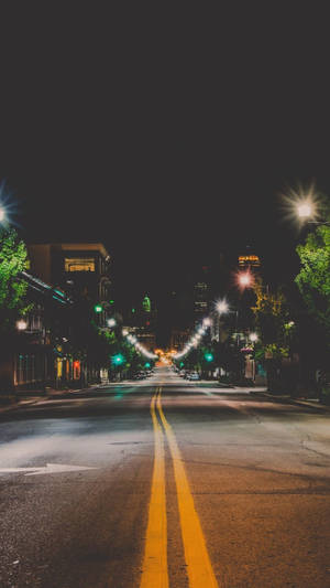 夜晚的城市街道，有發光的街燈和兩旁的樹木。