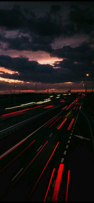 黃昏時分的高速公路，在色彩繽紛的多雲天空下，車燈形成光軌。