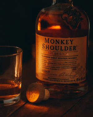 Monkey Shoulder威士忌瓶、玻璃杯和軟木塞在木桌上，溫暖昏暗的光線。