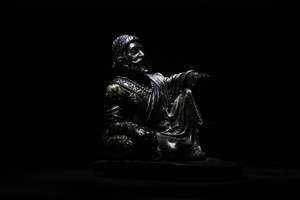 黑色雕像，鬍鬚男子穿長袍，被聚光燈照亮，背景黑暗