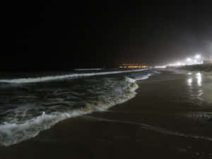 夜晚城市燈光下，海浪湧上黑暗的海灘。 — 夜晚 GIF 壁紙