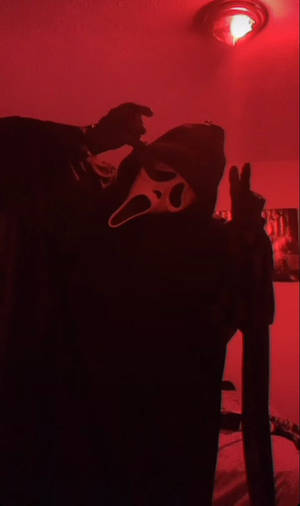 紅色燈光房間中戴著Ghostface面具的人物做出和平手勢。