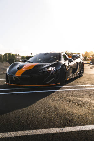 黑色McLaren跑車帶有橙色條紋，停在瀝青路上，夕陽西下。