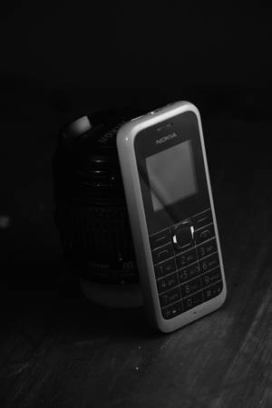 一部經典Nokia手機放在木桌上，旁邊是一個相機鏡頭。 — Nokia 壁紙