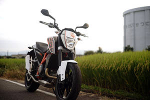 白色和橙色的電單車停泊在日本鄉村的稻田旁。