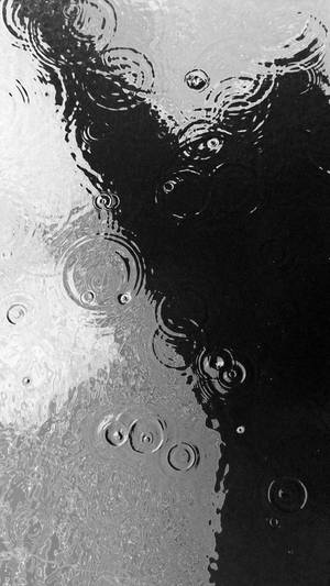 雨滴在潮濕玻璃表面形成漣漪的黑白影像。