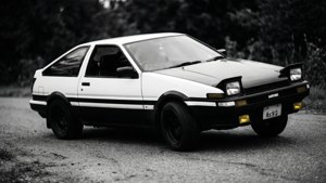 黑白豐田AE86 Corolla Levin停泊在碎石路上，後面有樹木
