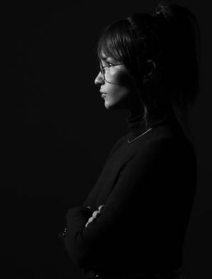 戴眼鏡、雙臂交叉的女性側面黑白攝影棚照。
