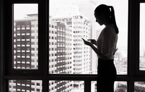穿著商務服裝的女性在都市窗邊看手機