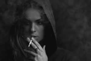 一個戴著帽子的女人在一張陰暗氣氛的黑白照片中吸煙。
