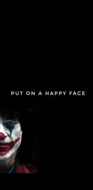 一個帶有紅色嘴唇和藍色眼淚的可怕小丑，從黑暗中的「put on a happy face」文字下方向上凝視。