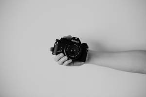 在簡約的攝影棚環境中，手拿著黑色 Nikon 相機。