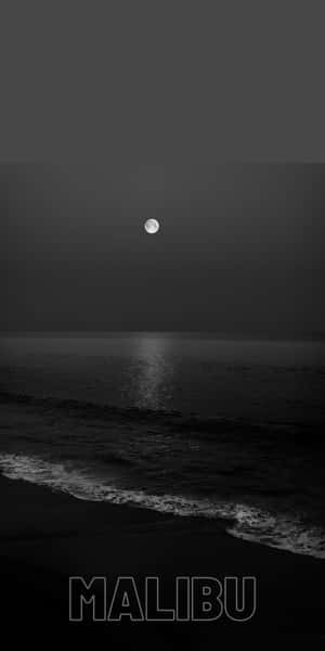 滿月照在黑暗的海洋上，在夜間海灘的水面上反射