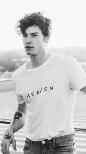 有紋身的年輕男子穿著印有 heaven 的白色T恤站在屋頂上。