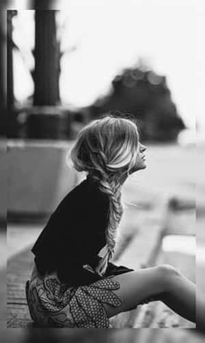 一位長辮子女士坐在長椅上，在黑白照片中仰望。