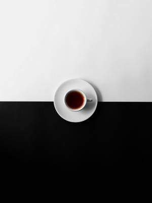 一個白色茶杯裝著深色茶，放在碟子上，背景為黑白兩色。
