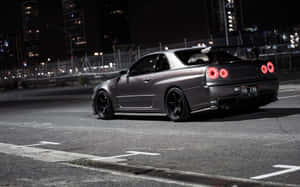 啞光灰色日產Skyline GT-R，紅色尾燈，夜晚停泊在城市街道上。