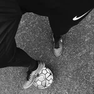 身穿黑色Nike裝備的人在瀝青上控制足球。