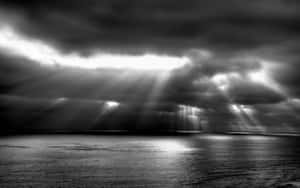 陽光光束穿透暴風雲，照射在平靜的海面上。 — 黑白 壁紙