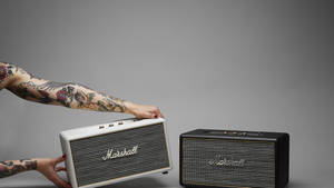 紋身的手拿著一個白色 Marshall 揚聲器在一個黑色旁邊。
