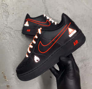 戴手套的手拿著一對黑色Nike運動鞋，帶有發光的橙色和白色細節。