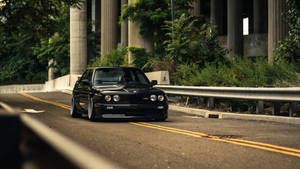 黑色BMW E30在帶有混凝土柱和綠植的高速公路上行駛