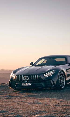 黑色 Mercedes-AMG GT 跑車停在日落時分的塵土飛揚的山丘上，背景有山脈。